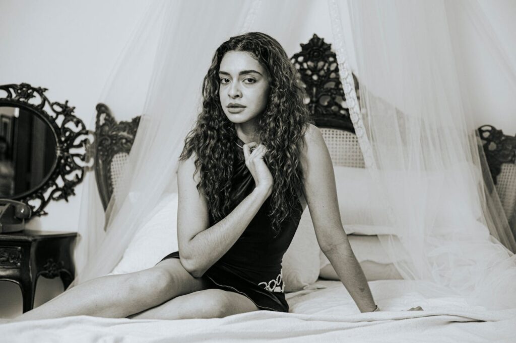A thoughtful woman poses elegantly on a vintage bed in a serene setting.